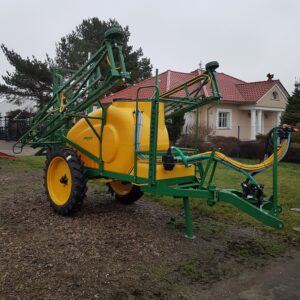 Żółto-zielony opryskiwacz rolniczy stojący na podwórku przed domem.