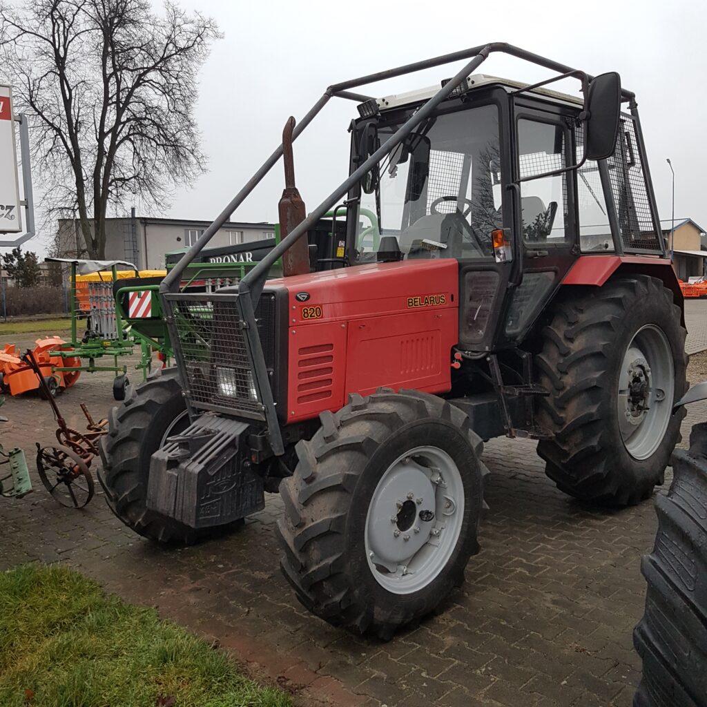 Czerwony traktor Belarus 820 stojący na placu z maszynami rolniczymi w tle.