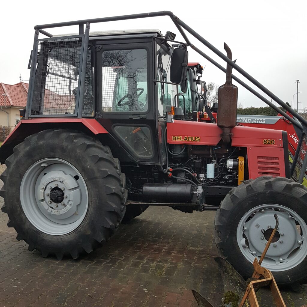 Czerwony traktor Belarus 820 zaparkowany na bruku.